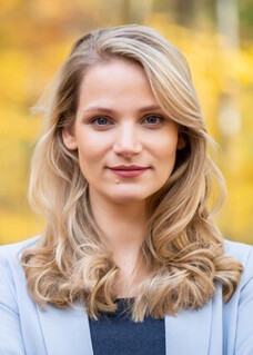 Frau Lissner mit langen blonden Locken, draußen mit herbstlichem Hintergrund.